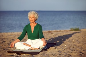 bigstock-Elderly-Woman-On-Beach-Meditat-52950844